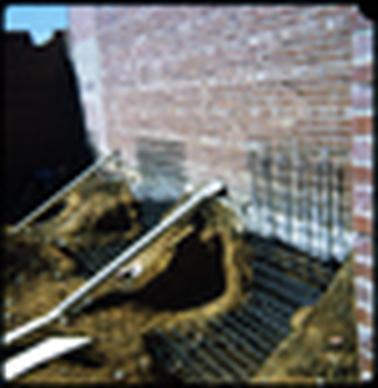 This shows a red brick wall at the back of a shop, and in the foreground are some metal grills, and sand. There are some building works in progress. 