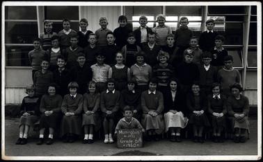 This shows 41 children in the school grounds. They are ranged in four tiers, so they can all be seen plainly. The child in the middle front row, a boy is holding a sign. It states: Mornington No:2033 Grade 6A 1960. The children are in various clothing, a few seem to have a uniform. 