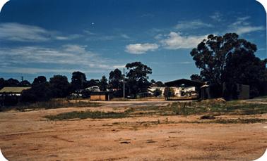 Vacant land with buildings among trees in the background.