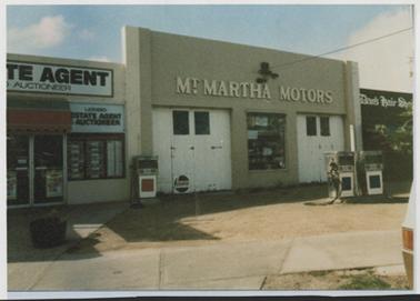 Image of Mt Martha Motors garage, brick construction, painted beige with 2 white painted double doors and 3 petrol bowsers