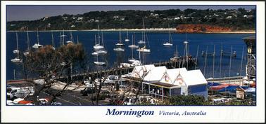This is a beautiful view of the water from the foreshore. It is taken near the Yacht Club between Mother’s Beach and the Pier. In the foreground are the tea rooms, painted blue, with their distinctive four pitched roof of white corrugated iron. There are many yachts on the bay, and some moored. In the background on the right is a glimpse of Shire Hall Beach, and the red cliff beyond. In the background is  Beleura Hill, which is mainly bush with some houses among the trees.