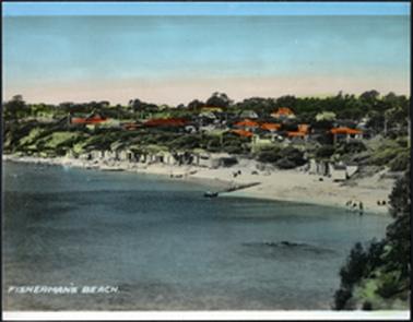 This is a view of the beach from the opposite headland. It shows several people on the beach in the distance, and there are many bathing boxes. The sea is very calm. There are lots of houses on the crest of the embankment.  