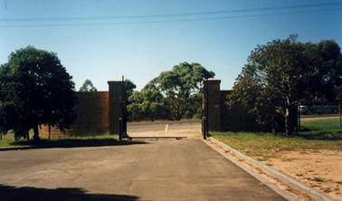 View of Balcombe Memorial gates and gate posts taken from inside the site. The main bitumen road outside is visible through the open gates. 