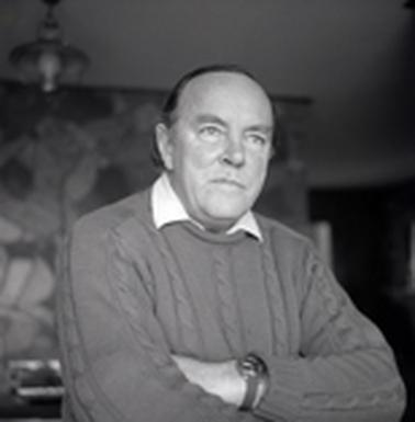 Portrait of upper torso of a maln wearing a hand knit jumper, his arms are folded .