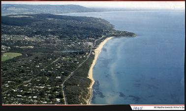This is a view from above showing a large area of Mt Martha. Port Philip Bay is on the right of the photo. The beach runs vertically from the bottom to the top of the picture. Arthur’s Seat can be seen in the back ground. 


