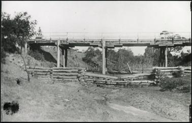 Image shows wooden trestle bridge over Tanti Creek in foreground log fence