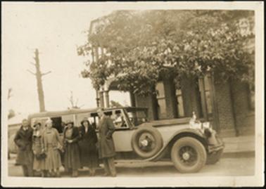 A close-up photo of a group of friends posing in front of their Packard car during their touring, the Royal Hotel behind them in photo 