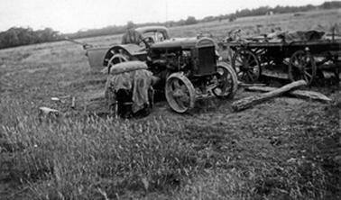 Tractor in paddock with utility truck to rear and beside a wagon. Unknown man sitting on the tractor.