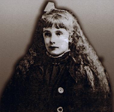 Head and shoulders portrait of young girl in a dark coloured high necked dress. There appears to be a dark coat with prominent buttons over the dress. She has a fringe  and very thick long curly hair covering her shoulders in front and with a bow in her hair.