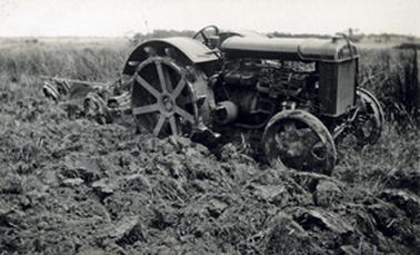 Tractor and attached plough standing in partially ploughed paddock.