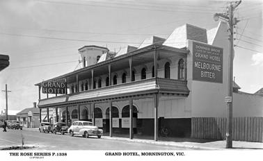 This shows the Grand Hotel front onto Main Street. There is a large sign on the side of the Hotel “Downes Bros, late of Hay N.S.W. Grand Hotel, Melbourne Bitter”. There are 3 cars parked outside the Hotel. There are verandahs on both the ground, and upper floors. This shows 6 arches on the Hotel, and the tower has a flat top. To the left of the photo and the Hotel appears to be a private residence.This is a Rose postcard, series P.1338.