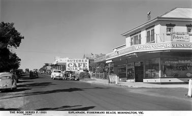 To the right of this picture is a two storey rendered building with a verandah and it is marked Martin’s Corner, and underneath the sign it is marked Licensed Real Estate & Insurance Agent. The ground floor is obviously a shop. Part of the same building is a General Store, the phone number is shown as number 88. Next to that is the Fruit and Vegetable shop. In the centre of the photo is a Butcher, and Cafe Milk Bar. A sign for Sennit’s Icecream is visible. To the right of the picture the road is shown and several vehicles are parked, and some are travelling. 